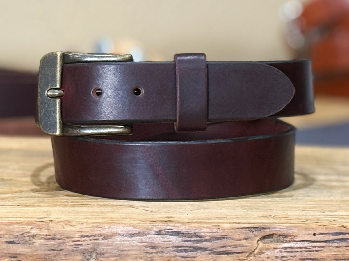 Close-up of the dark burgundy full-grain latigo leather surface, finished edge, keeper, and vintage brass buckle
