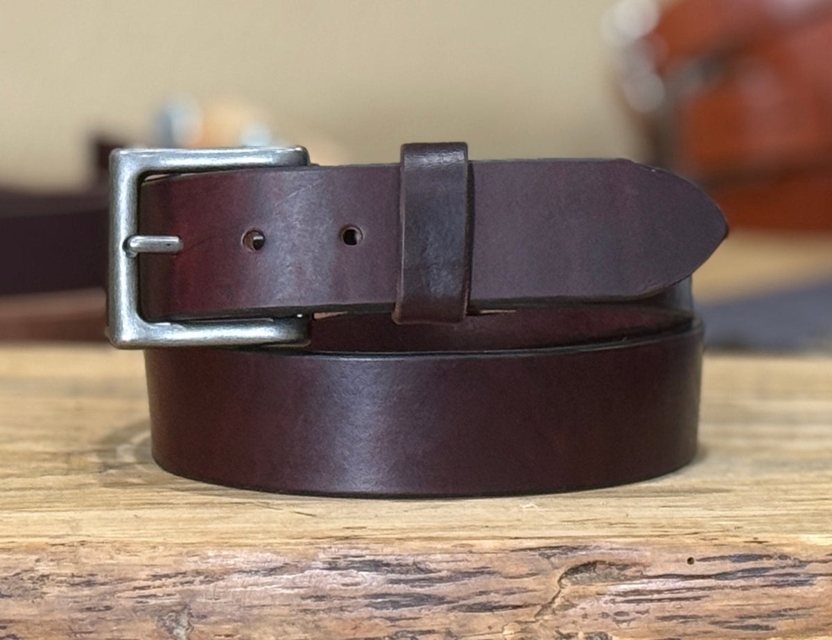 Burgundy leather belt with silver buckle on a wooden surface