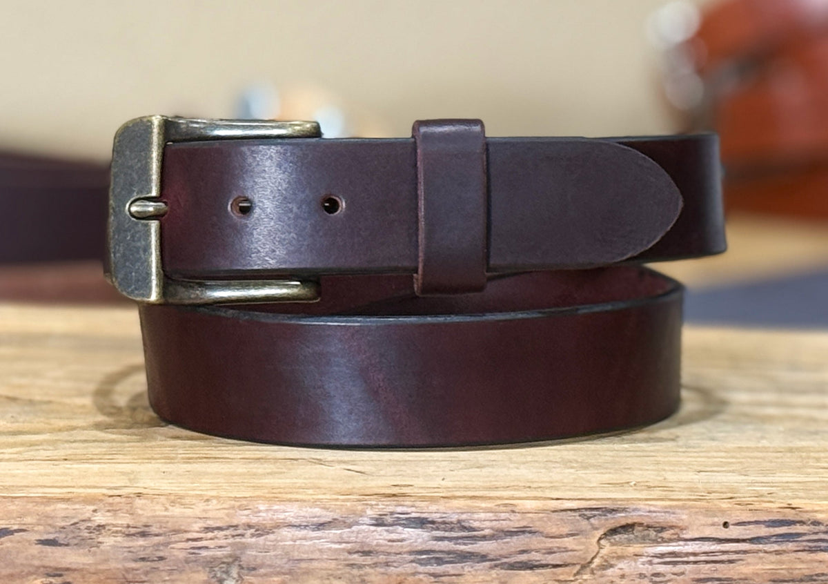 Burgundy leather belt with brass buckle on a wooden surface