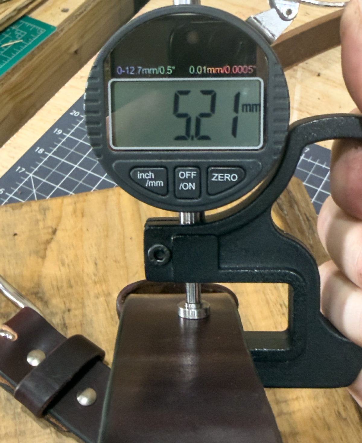 Digital caliper measuring a leather strap on a wooden surface