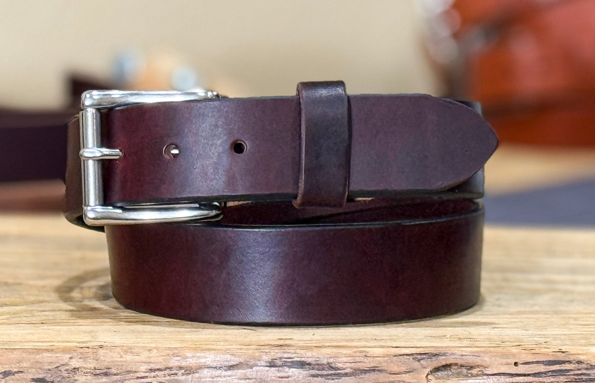 Burgundy leather belt with silver buckle on a wooden surface