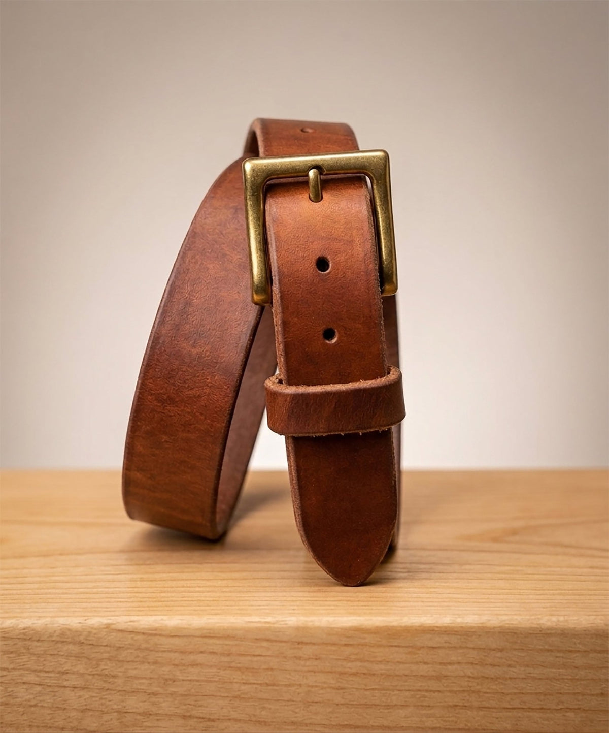 Brown leather belt with brass buckle on a wooden surface