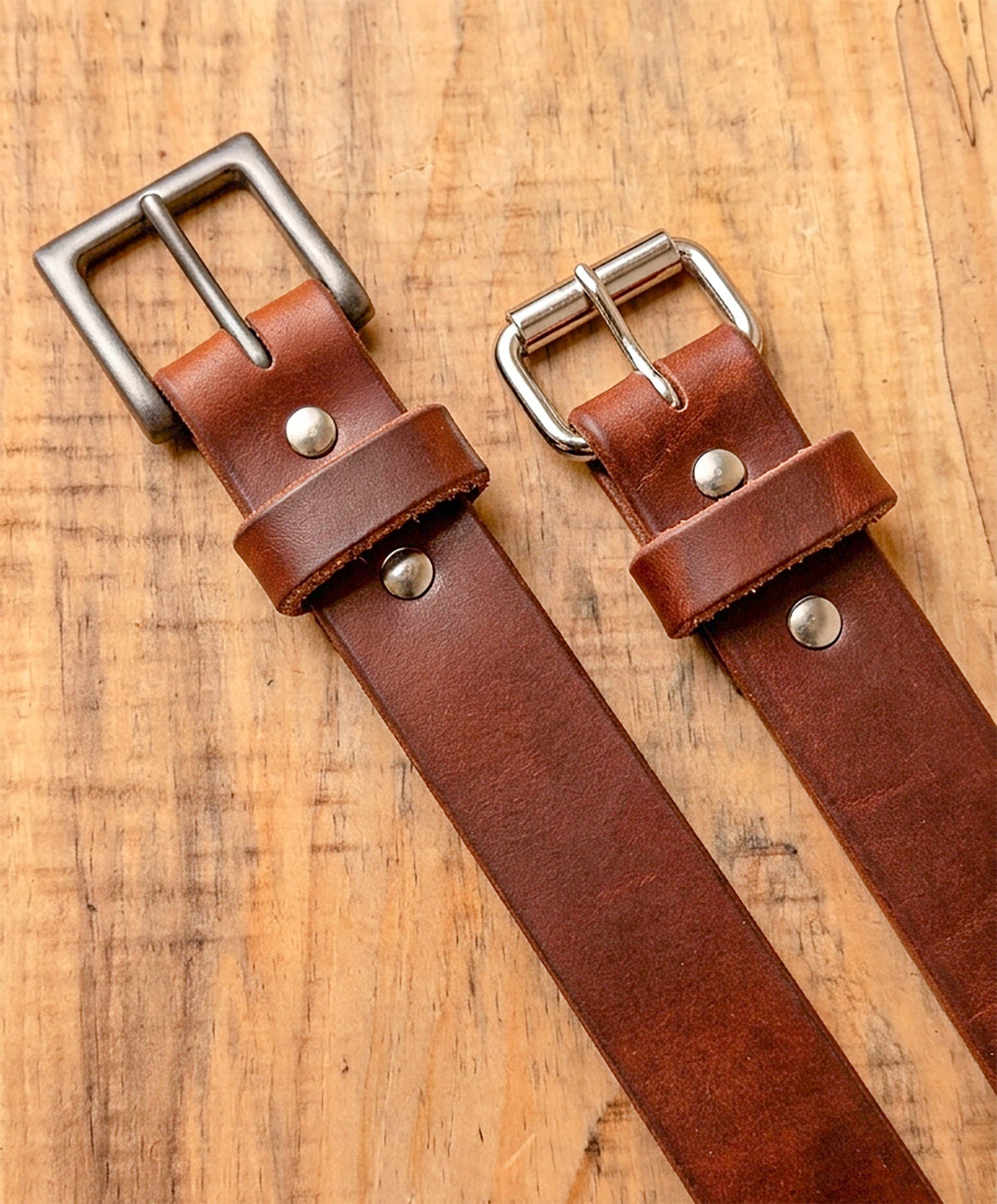 Two brown leather belts with silver buckles on a wooden surface