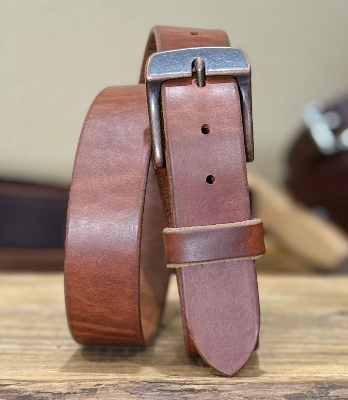 Brown leather belt with a silver buckle on a wooden surface