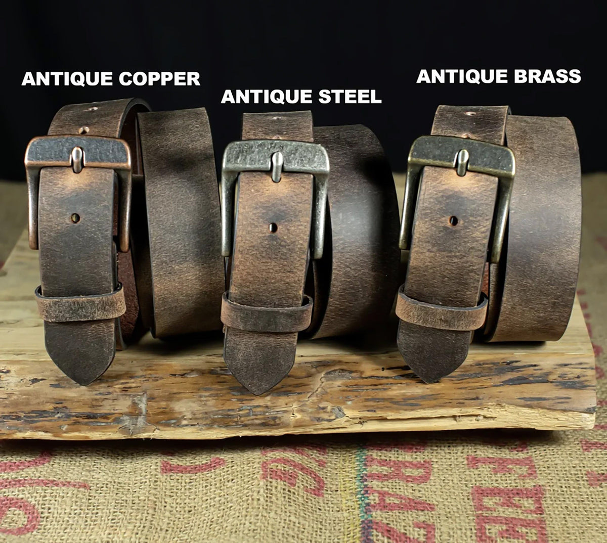 Three leather belts with different metal buckles labeled 'Antique Copper', 'Antique Steel', and 'Antique Brass' on a rustic background.
