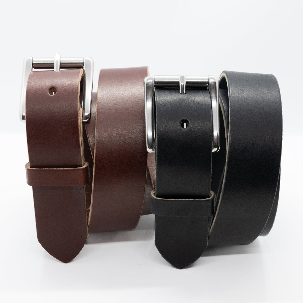 Black and brown Maverick Amish-made raw-edge leather belts standing together with roller buckles on white.