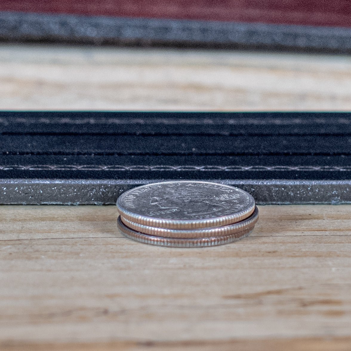 Edge close-up of black and brown Rancher embossed-lines leather belts with stacked coins for a thickness comparison.