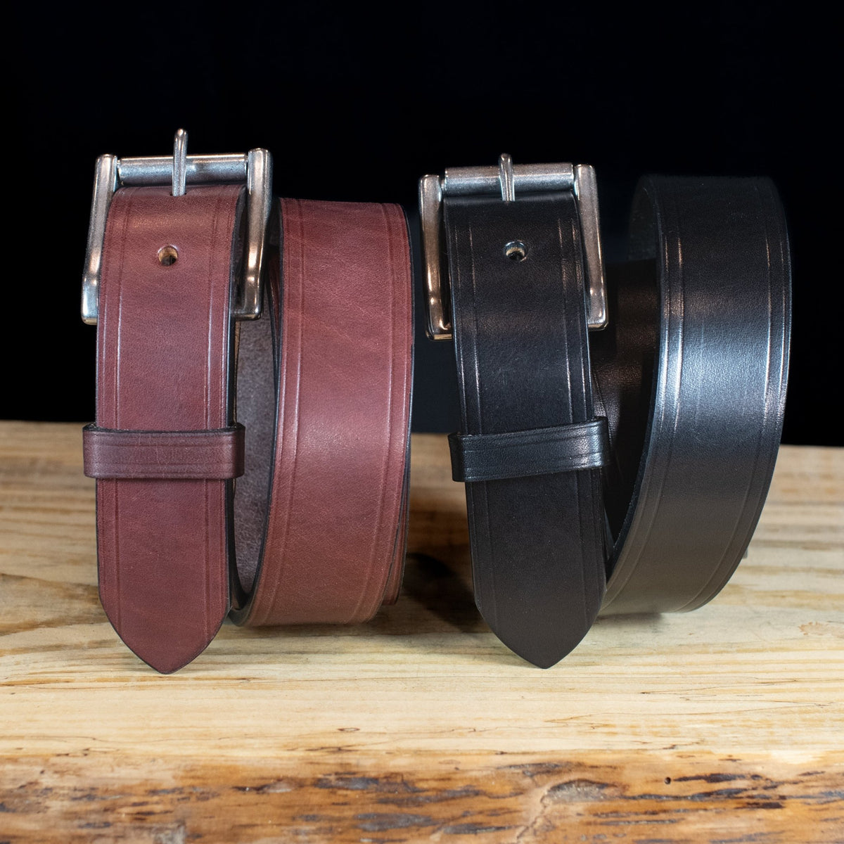 Black and brown Wrangler creased-edge leather belts standing together against a dark background.