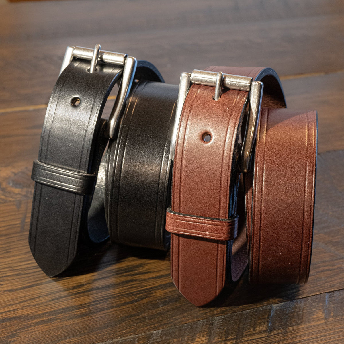 Black and brown Wrangler creased-edge leather belts standing together with silver roller buckles on wood.