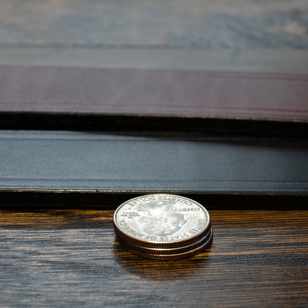 Black and brown Wrangler creased-edge leather belt straps beside stacked coins for a thickness comparison.