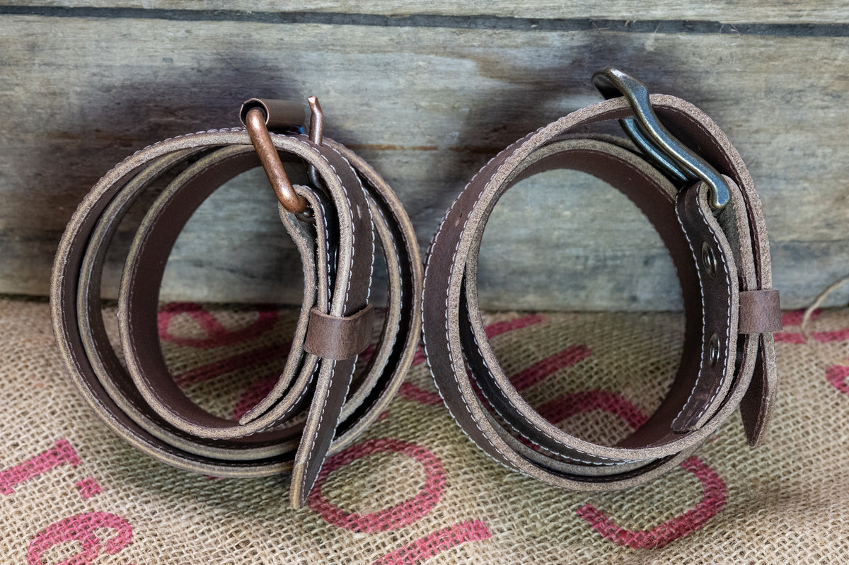 Two leather belts  on a rustic wooden surface with burlap fabric underneath.