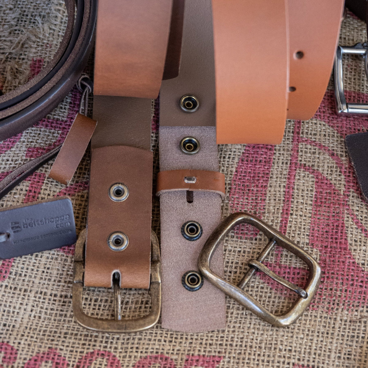 Close-up of leather belts with brass buckles on a textured fabric background
