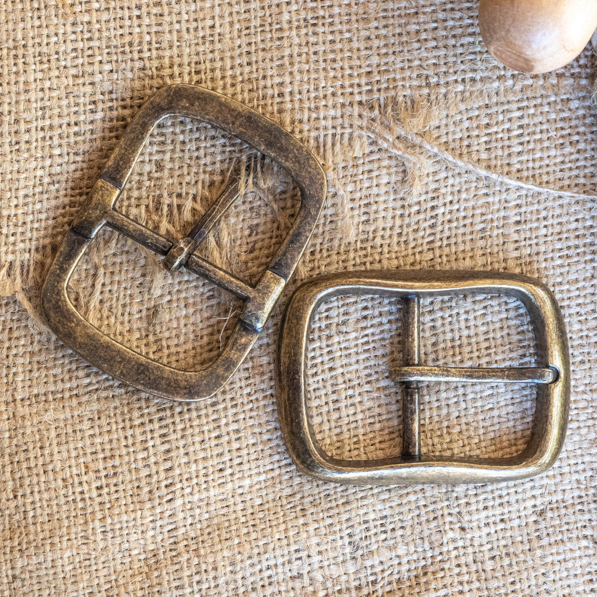 Two brass belt buckles on a burlap background