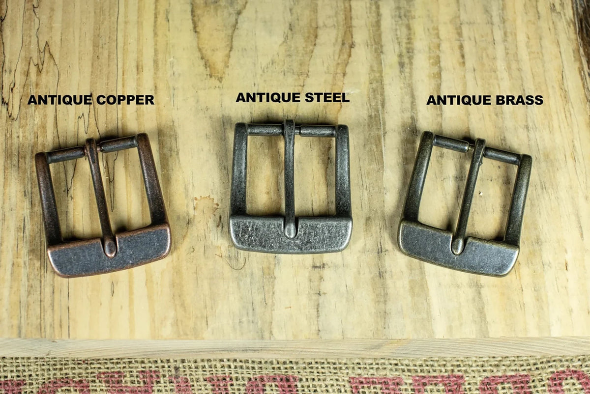 Three metal buckles labeled 'Antique Copper', 'Antique Steel', and 'Antique Brass' on a wooden surface.