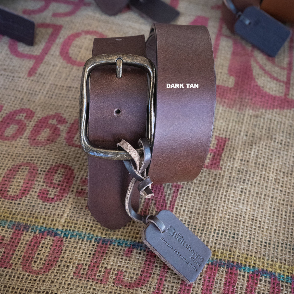 Brown leather belt with silver buckle and tag on a textured fabric background