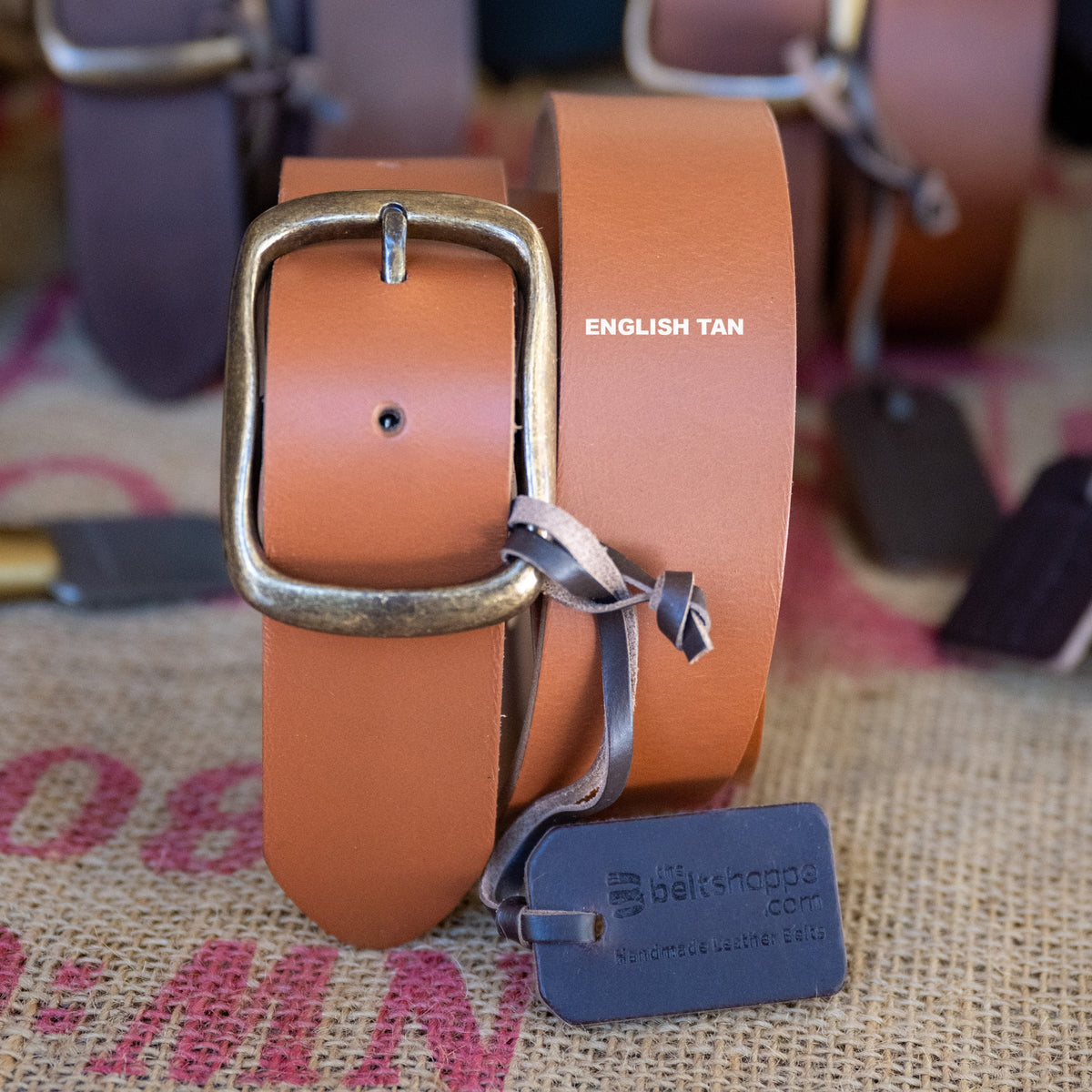 Brown leather belt with brass buckle on a textured surface, featuring 'English Tan' text.