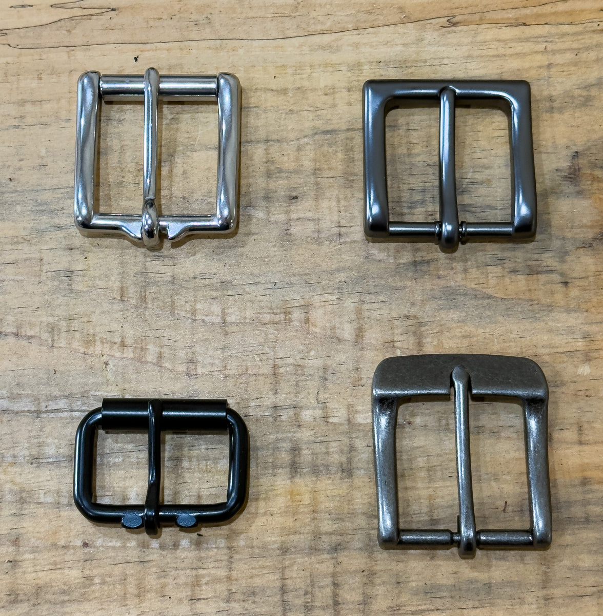 Four metal buckles of different styles and colors on a wooden surface