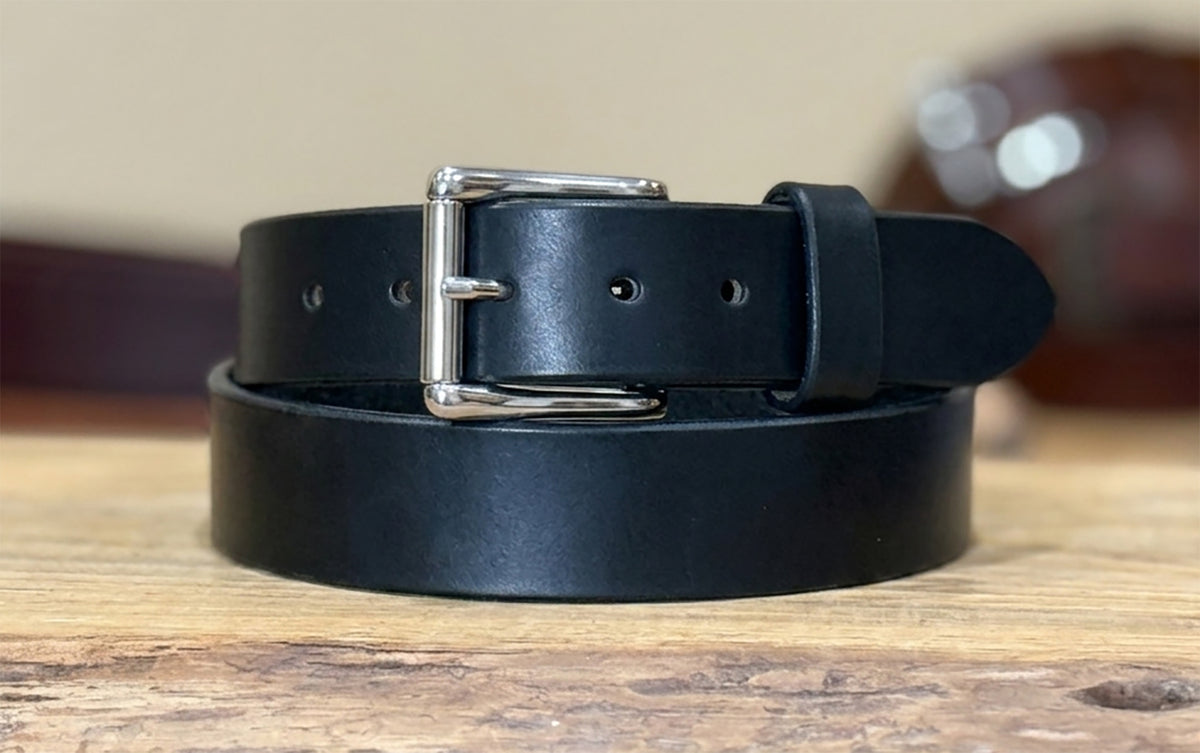 Black full grain harness leather belt with a stainless steel roller buckle on a wooden surface