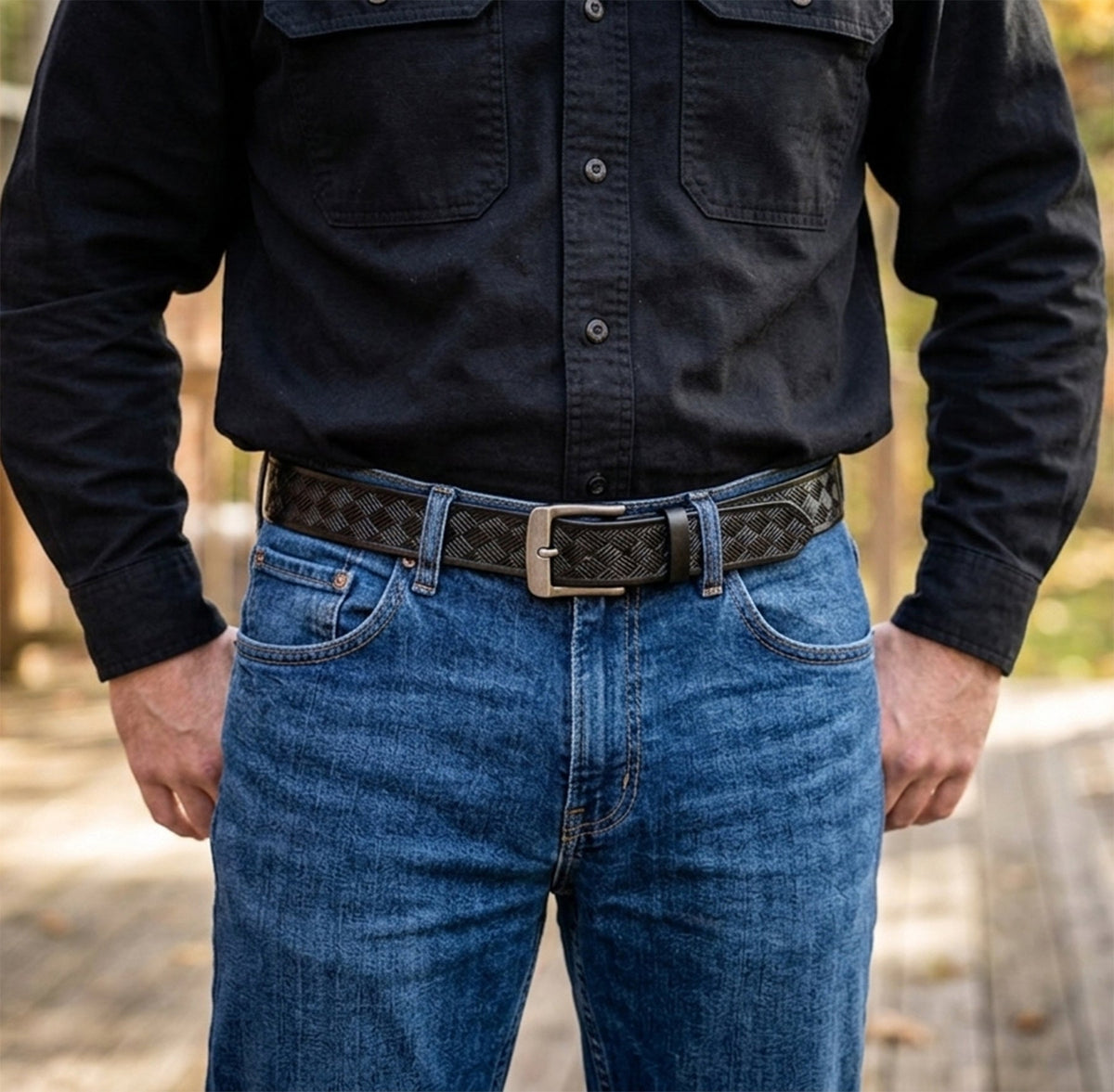 Black embossed steer hide leather belt worn with blue jeans and a black shirt, showing its basketweave pattern and rectangular buckle.