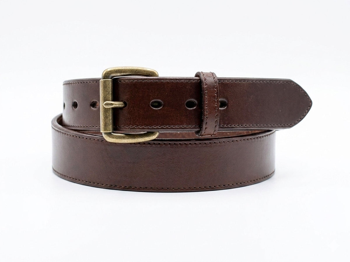 Brown stitched-edge steer hide leather belt coiled on white, showing its brass-tone buckle, matching keeper, and pointed tip.