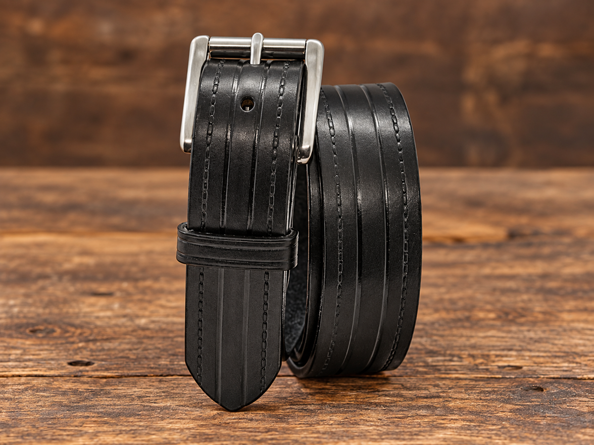 Black Rancher 1.5-inch Amish-made heavy-duty leather belt with embossed lines and silver roller buckle on a rustic wood surface.