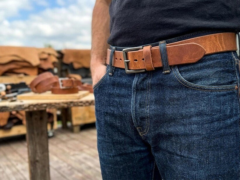 Russet harness leather belt worn with blue jeans in a leather workshop.