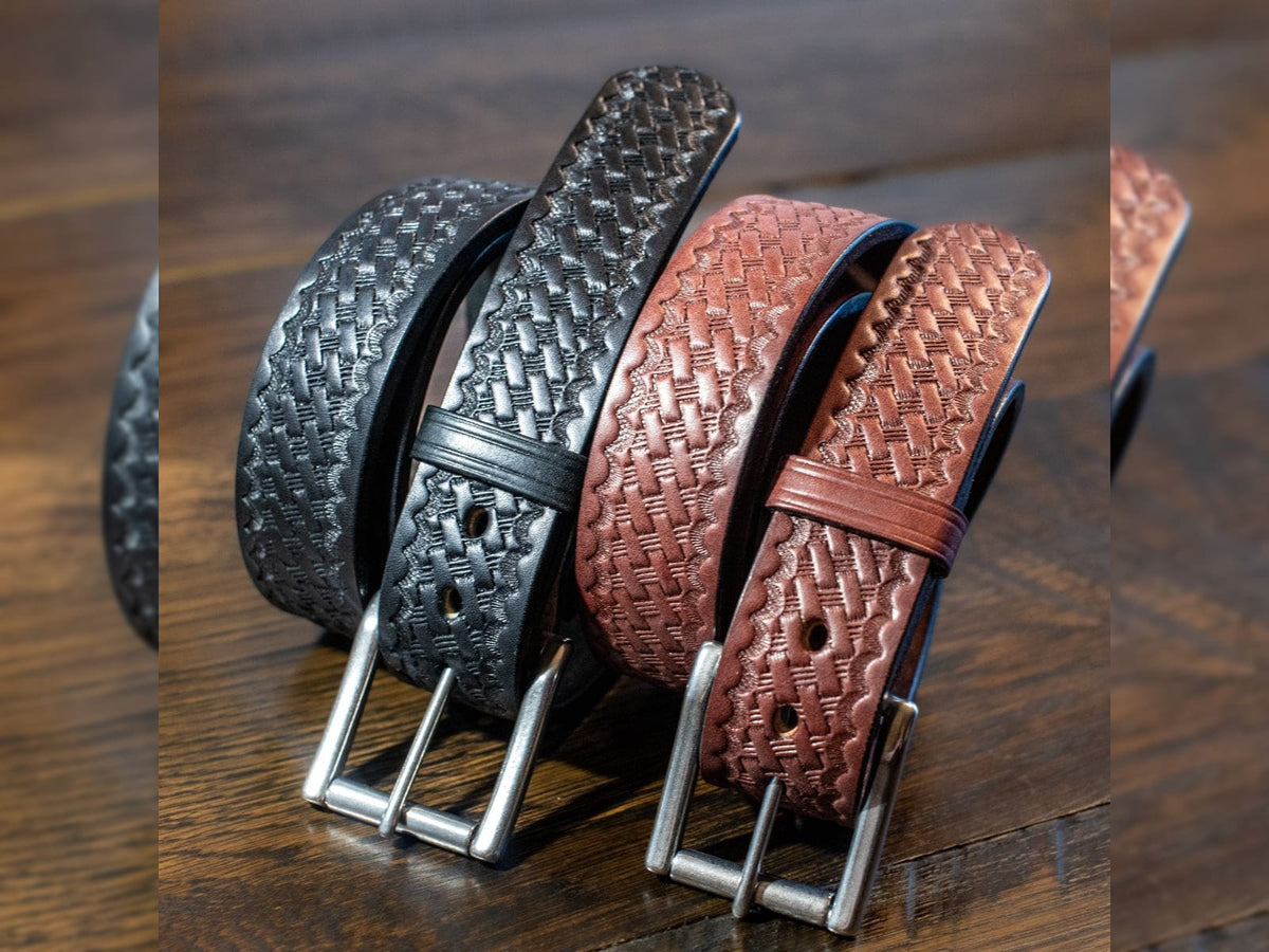 Black and brown 1.5 inch full grain harness leather basket weave belts with textured embossed straps and roller buckles on wooden surface.