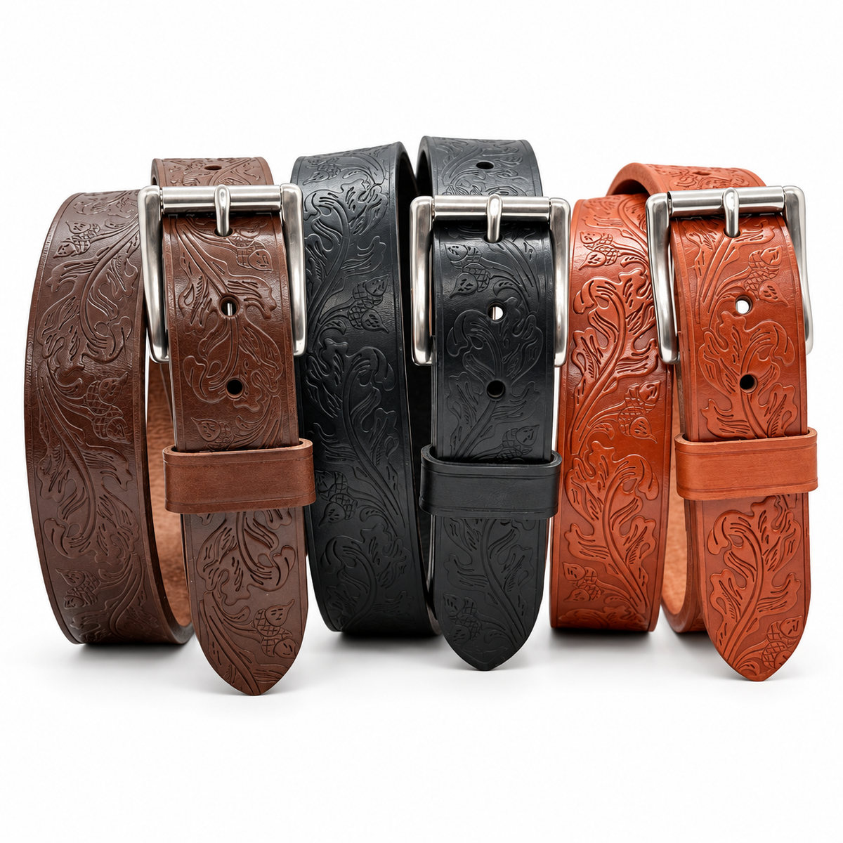 Brown, black, and tan oak leaf and acorn embossed harness leather belts standing upright with stainless steel roller buckles.