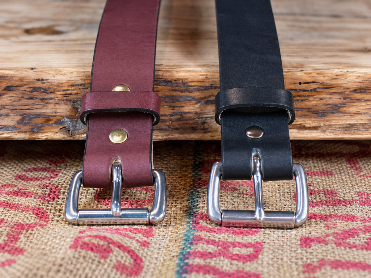 Black and brown Workhorse Amish-made full-grain leather belts with silver roller buckles on a textured fabric background.