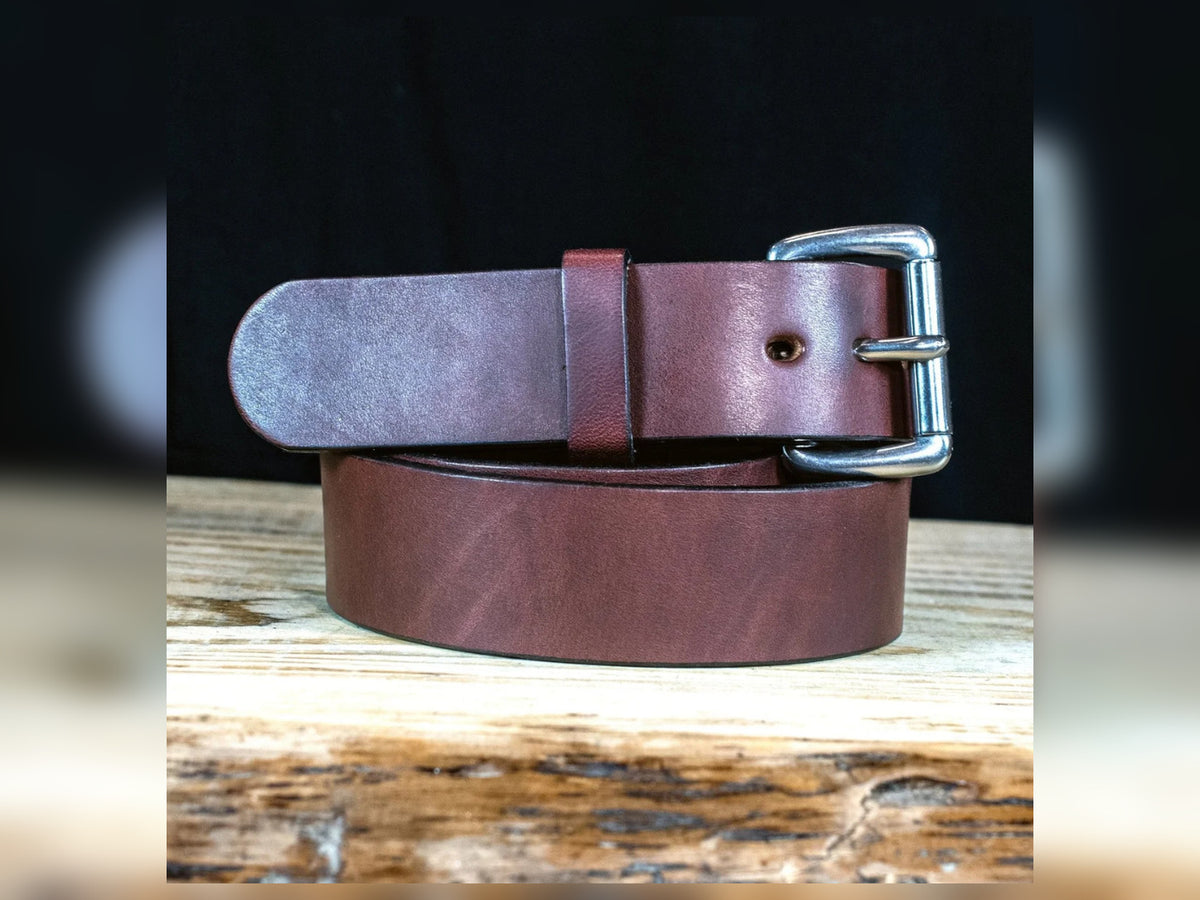 Brown Workhorse thick full-grain Amish-made leather belt with silver roller buckle on a rustic wooden surface.