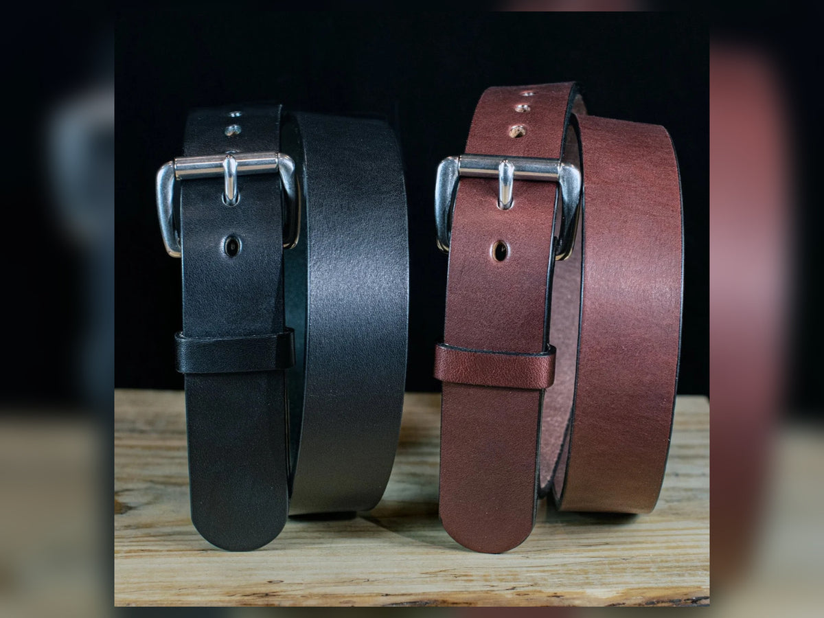Black and brown Workhorse Amish-made thick full-grain leather belts with silver roller buckles on a rustic wooden surface.