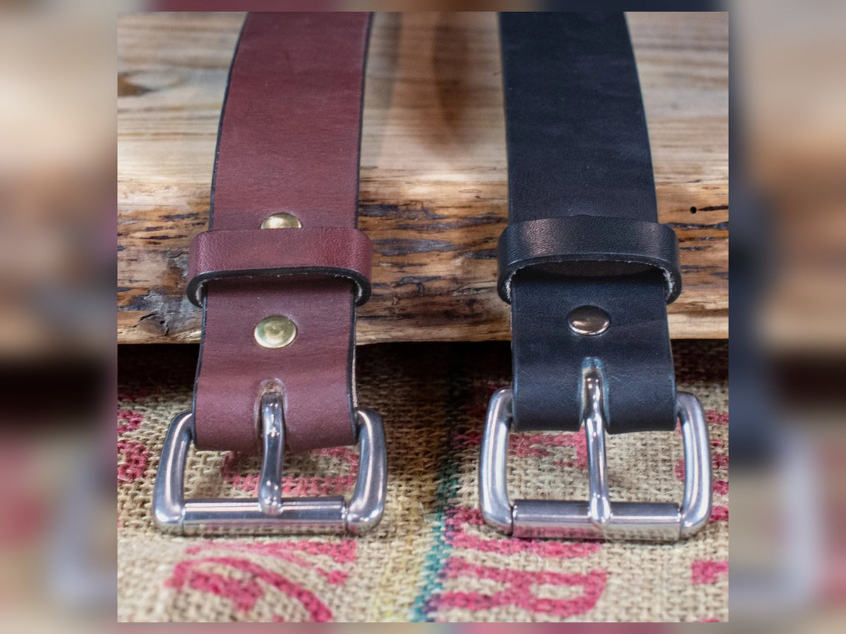 Black and brown Workhorse Amish-made full-grain leather belts with silver roller buckles on a textured fabric background.