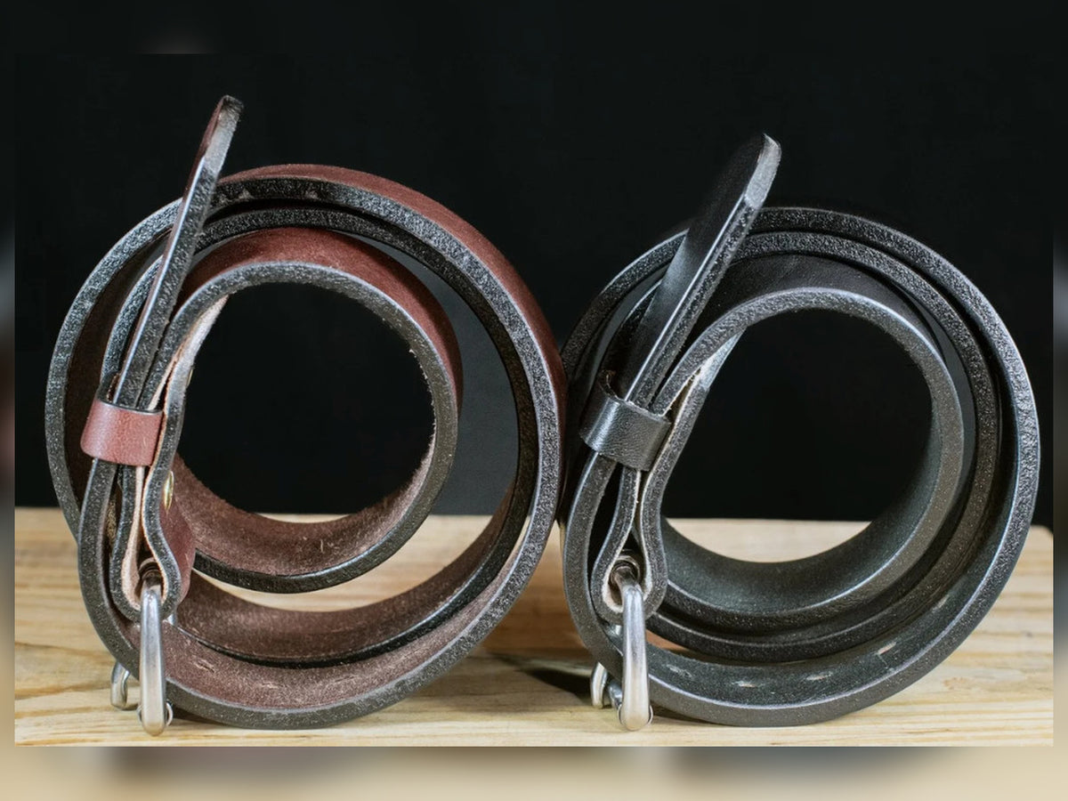 Side view of black and brown Workhorse full-grain leather belts showing their substantial leather thickness on a wooden surface.